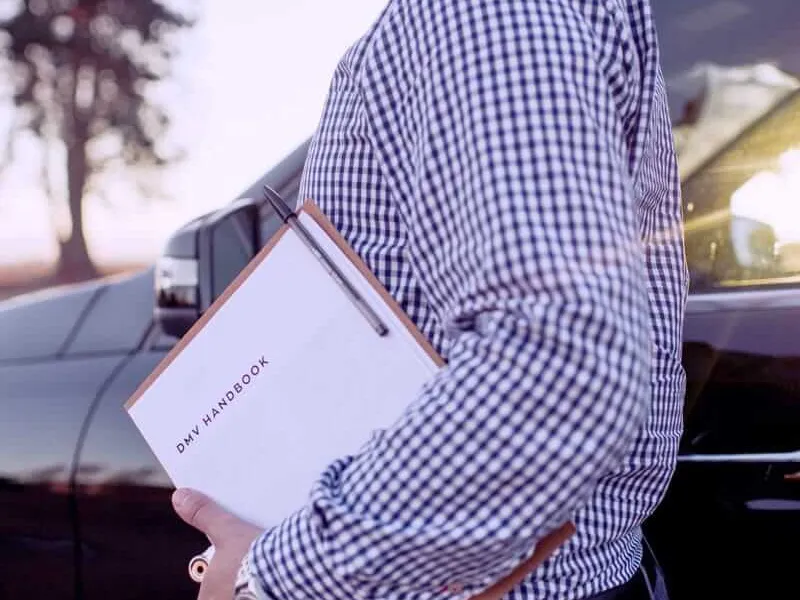 A driving instructor standing beside a car with a lesson clipboard