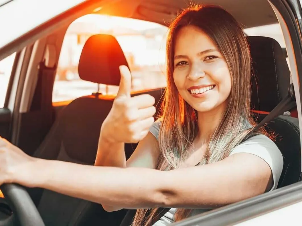 A smiling learner driver giving a thumbs up from the driving seat