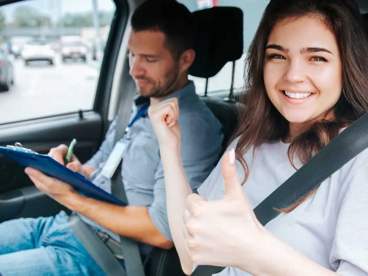A learner driver giving a thumbs up after a lesson, with an instructor taking notes